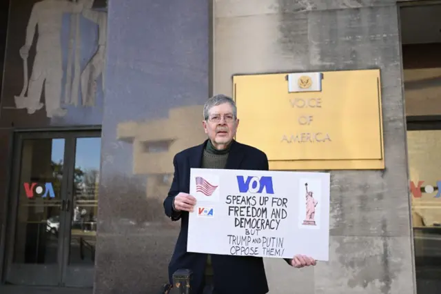 Una persona sostiene un cartel que dice que la VOA habla por la libertad y la democracia en el mundo. 