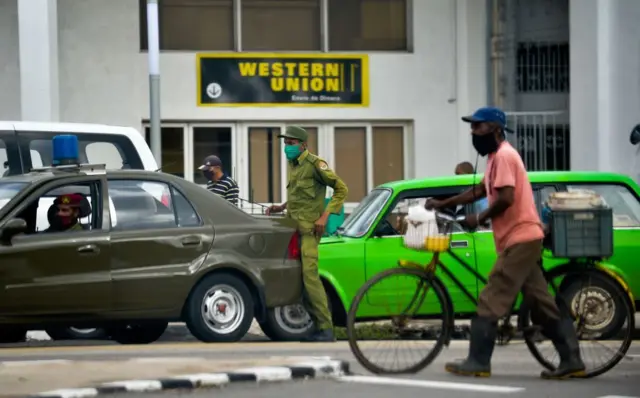 Autos y personas parados en una calle donde se ve una sucursal de Western Union en La Habana. 